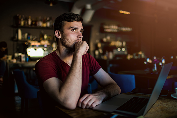 Jeune rédacteur web en t-shirt rouge, assis devant son ordinateur, réfléchissant au titre de son article