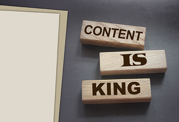 « CONTENT IS KING » écrit sur trois briques de bois à côté de feuilles de papier, sur fond marron