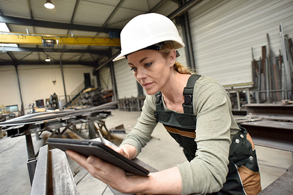 Femme avec un casque blanc, utilisant un logiciel de GMAO, dans un atelier industriel